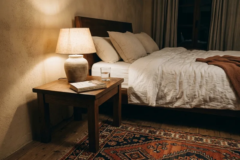 Rincón de cama completo con lámpara encendida, libro abierto y vaso de agua