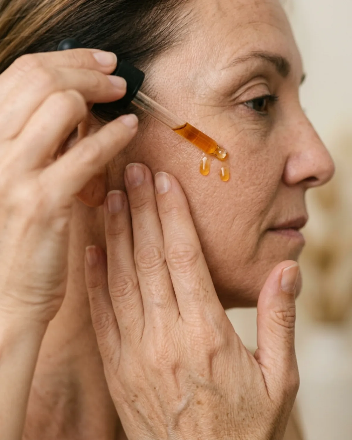 Mujer adulta de manos cuidadas aplicando crema reparadora sobre el dorso de la otra mano, plano detalle, luz calida de tarde.
