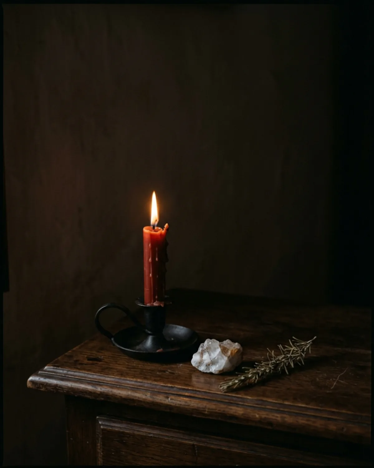 Vela blanca de cera encendida sobre mesa de madera oscura, junto a una libreta y una taza